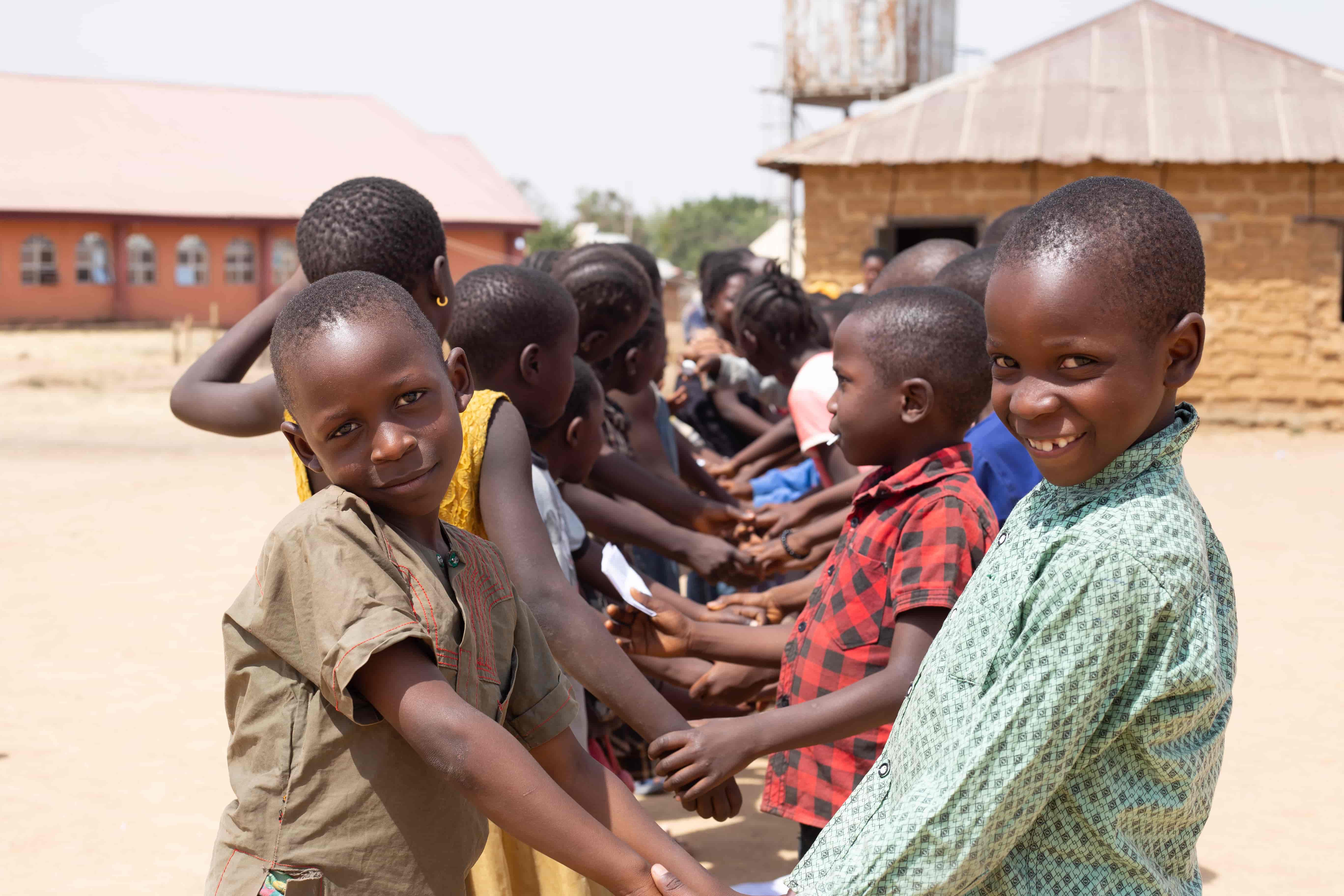 Children holding hands in a line during an outdoor community activity on an open field in Plateau State.