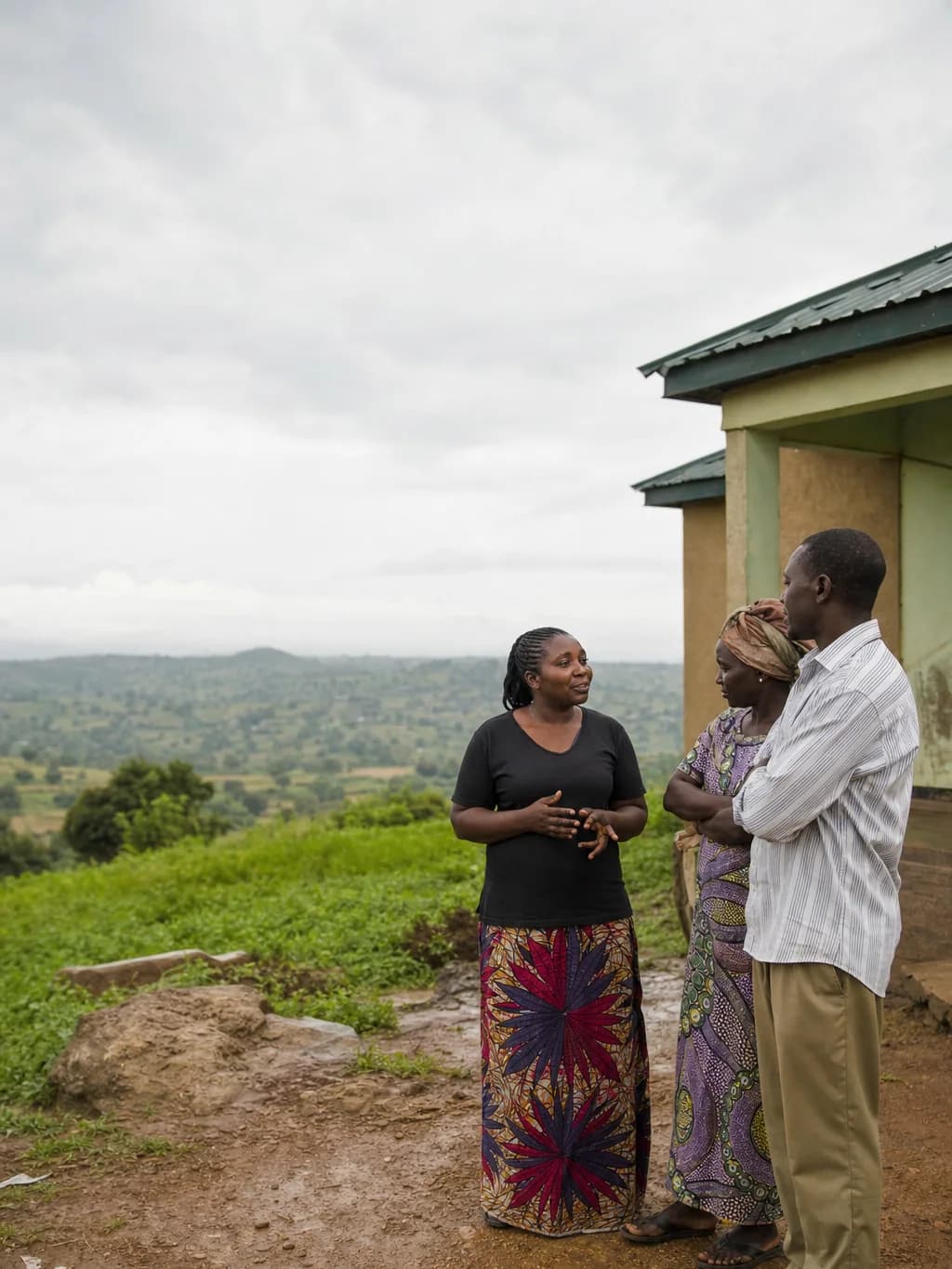 A community health worker speaks with two residents outdoors in a green Plateau landscape.