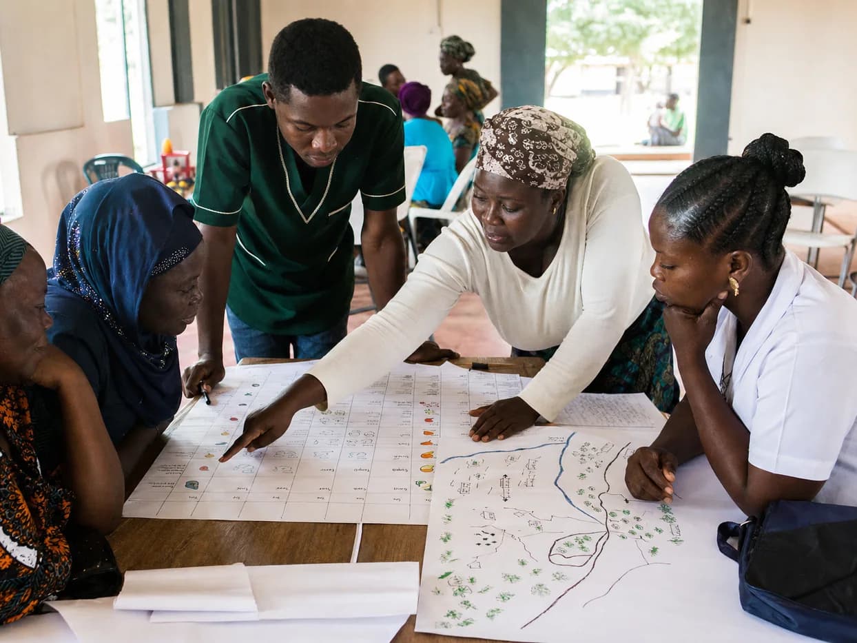 Community members and a health worker review a seasonal calendar and hand-drawn local map together.